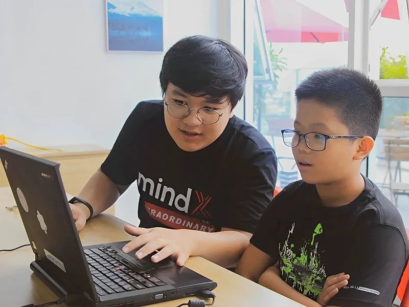 Một người lớn đang chỉ cho trẻ em về màn hình máy tính, minh họa việc học hỏi về không gian mạng.