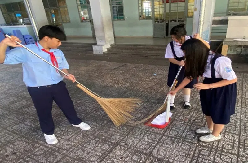 Một nhóm học sinh trung học cơ sở đang cùng nhau dọn dẹp khu vực hành lang, có cây xanh